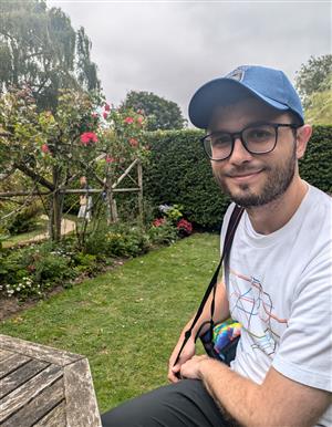 Jesse Richmond wearing a blue baseball cap with grass, flowers, and shrubs in the background